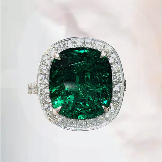 Photographie d’une bague sertie griffes, ornée d’une émeraude centrale entourée de diamants blancs.